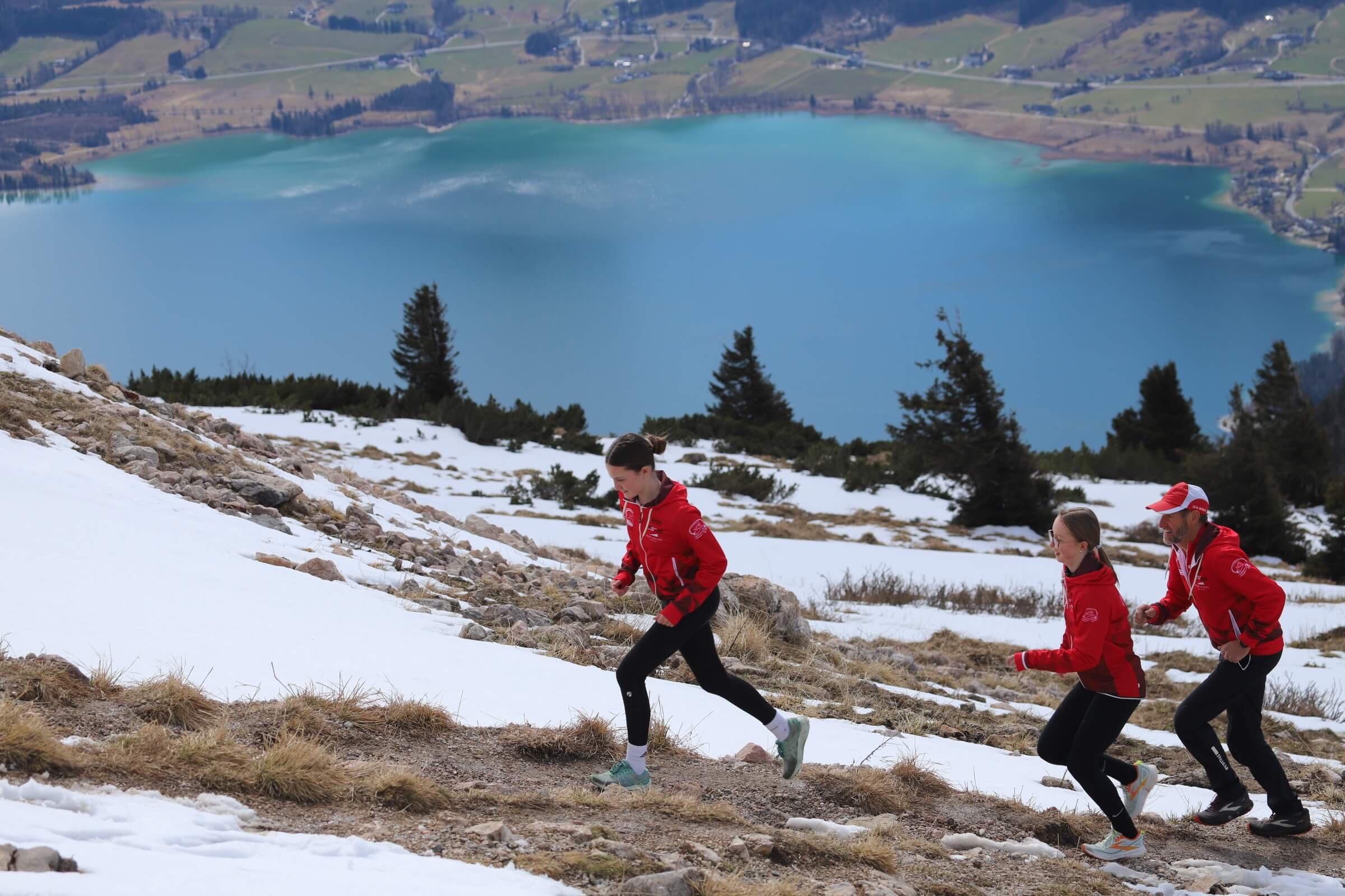Zwei Jugendliche und ein Trainer laufen auf dem Berg mit dem Wolfgangsee im Hintergrund
